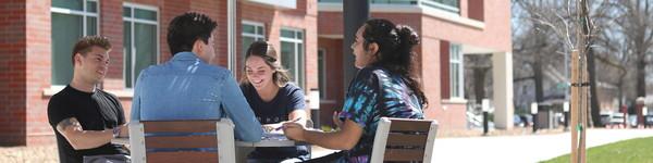 On an early spring day, four students sit outside Acklie Hall at a table with an umbrella.